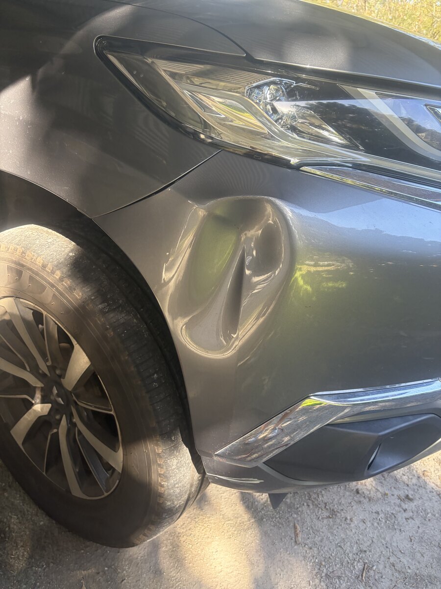 Deep dent creased into the plastic front bumper corner of a grey Mitsubishi SUV